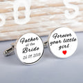 A pair of round white cufflinks with silver-toned metal edges and backs, featuring black script text. One cufflink reads 'Father of the Bride 26.09.2018' and the other 'forever your little girl' and a red heart.