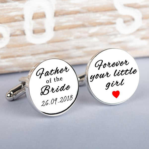 A pair of round white cufflinks with silver-toned metal edges and backs, featuring black script text. One cufflink reads 'Father of the Bride 26.09.2018' and the other 'forever your little girl' and a red heart.