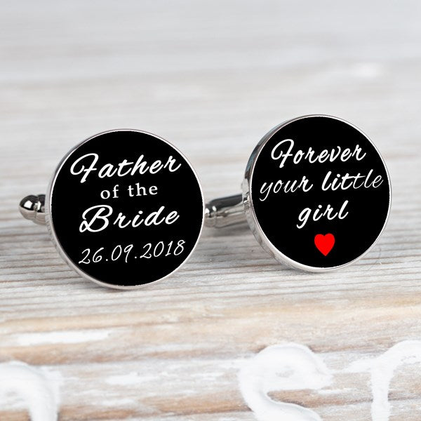 A pair of round black cufflinks with silver-toned metal edges and backs, featuring white script text. One cufflink reads 'Father of the Bride 26.09.2018' and the other 'forever your little girl' and a red heart.