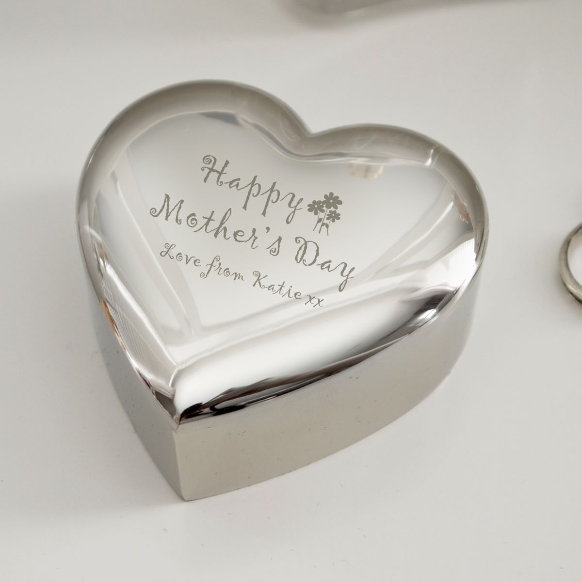 Heart-shaped silver trinket box with engraved message on a light background