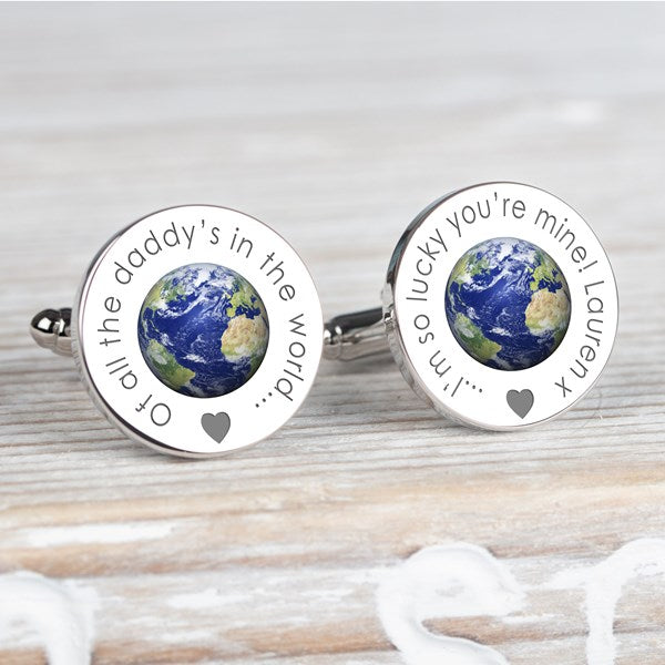 A pair of round silver cufflinks featuring a detailed globe of Earth in the centre, surrounded by engraved personalised text 'Of all the daddy's in the world..' on one and '...I'm so lucky you're mine!  Lauren x' on the other and a small heart, displayed on a neutral grey surface.