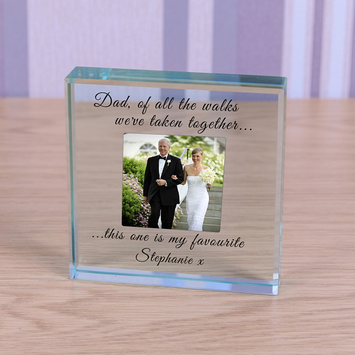 A personalised clear square glass block display on a light wood surface, featuring a photo of a bride and father, text reading 'Dad, of all the walks we've taken together...... this one is my favourite Stephanie x'.
