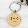 Wooden keychain with engraved initials and date on a white marble surface
