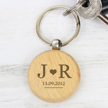 Wooden keychain with engraved initials and date on a white marble surface