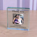 A personalized clear glass keepsake photo block on a light wood tabletop. The block is engraved with 'Thank You' at the top and 'Samantha FOR BEING OUR BRIDESMAID' at the bottom, featuring a custom photo of a bride and bridesmaid.