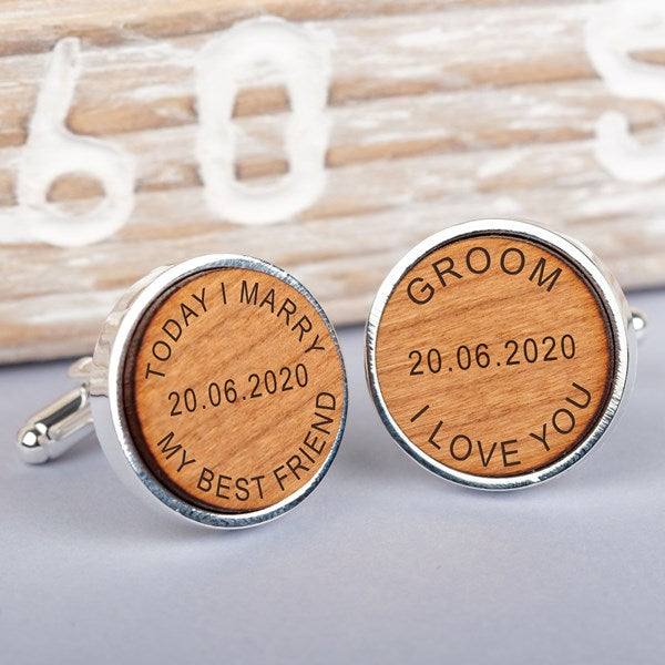 A pair of round silver cufflinks with engraved light brown wooden faces. One cufflink is engraved with 'TODAY I MARRY MY BEST FRIEND' and a date in the middle the other 'GROOM I LOVE YOU' and the same date.
