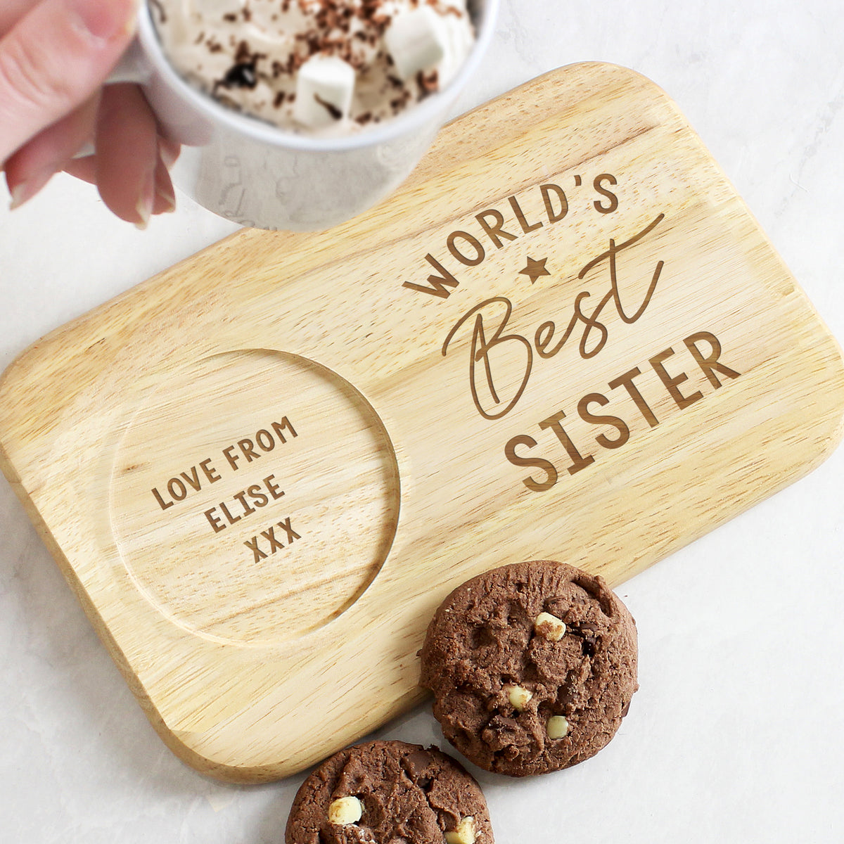 Wooden coaster with 'World's Best Sister' engraving, surrounded by cookies and a mug.