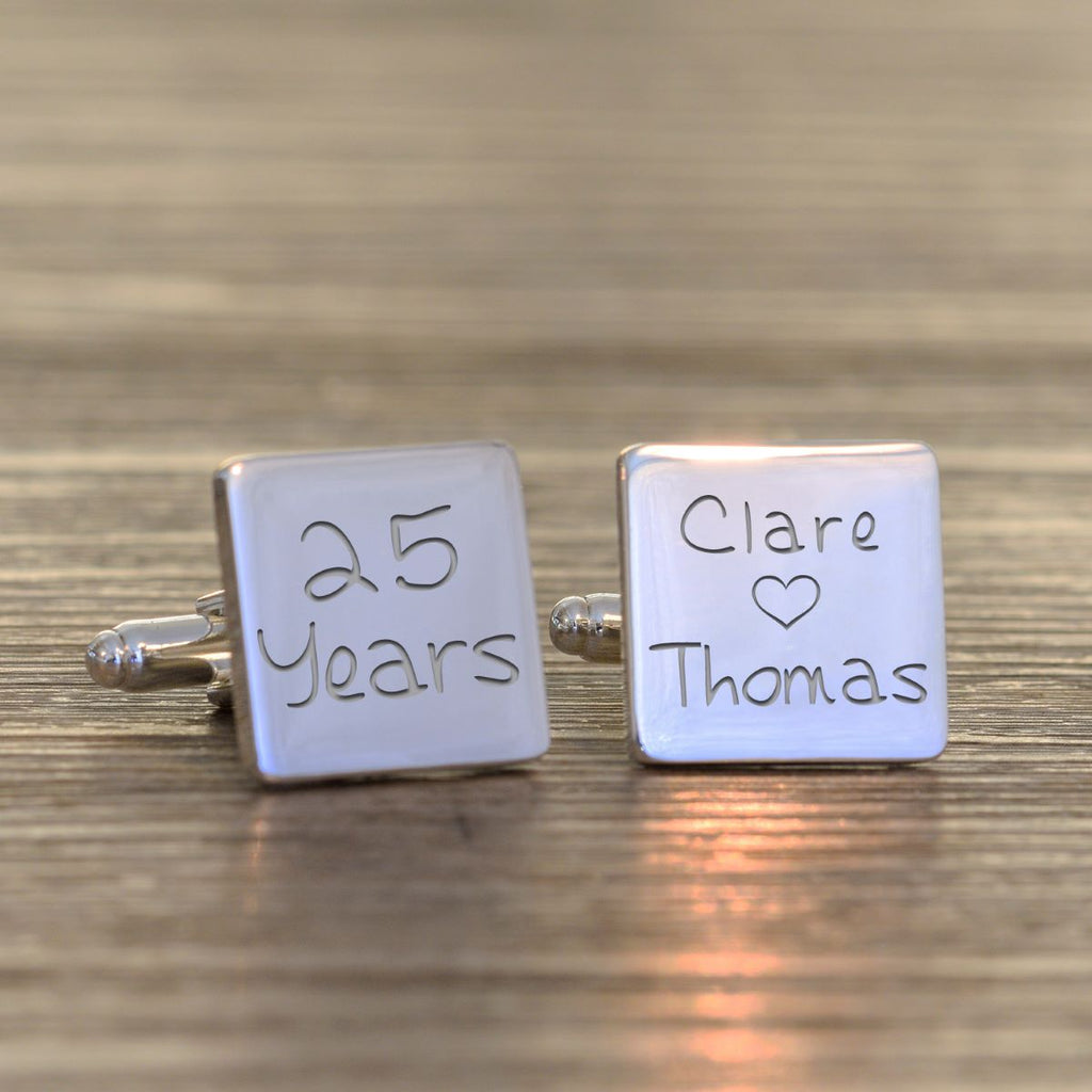 A pair of square silver cufflinks engraved with personalized names and milestones, one reading '5 Years' and the other 'Julia Michael' with a small heart, displayed on a wooden surface.