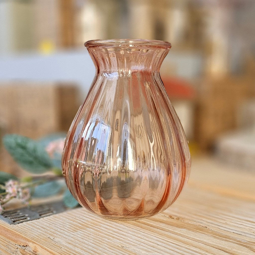 Pink glass ribbed vase on a wooden surface with a blurred background
