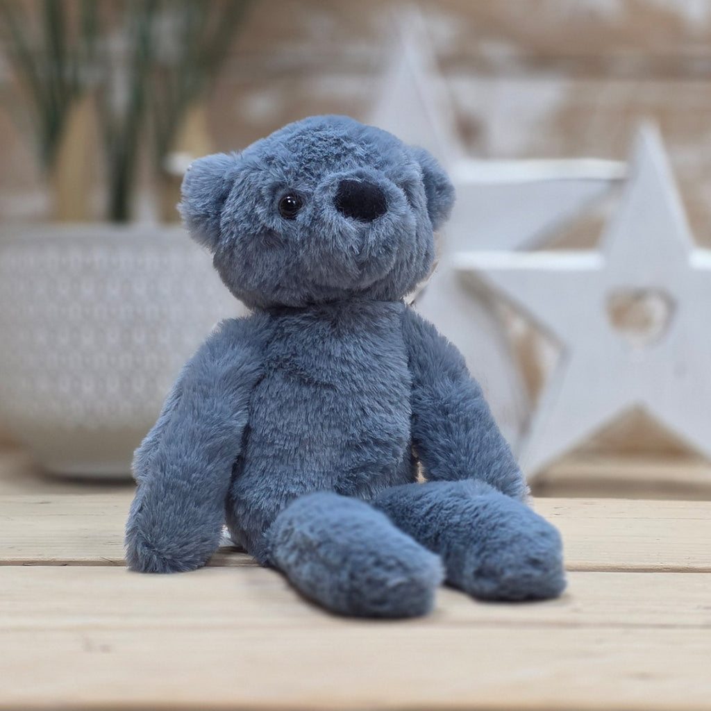 A blue soft fuzzy plush teddy bear toy, with black eyes and nose, on a wooden surface with a blurred star-shaped object in the background
