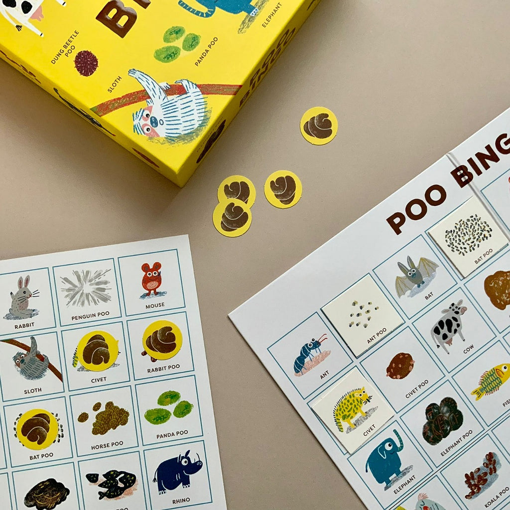 A children's board game called Poo Bingo, showing a yellow box, two printed activity sheets with animal poop illustrations, and several loose circular poop tokens on a beige surface.