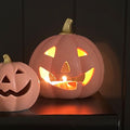 Two ceramic pumpkins with carved faces, one lit from within, on a dark background.