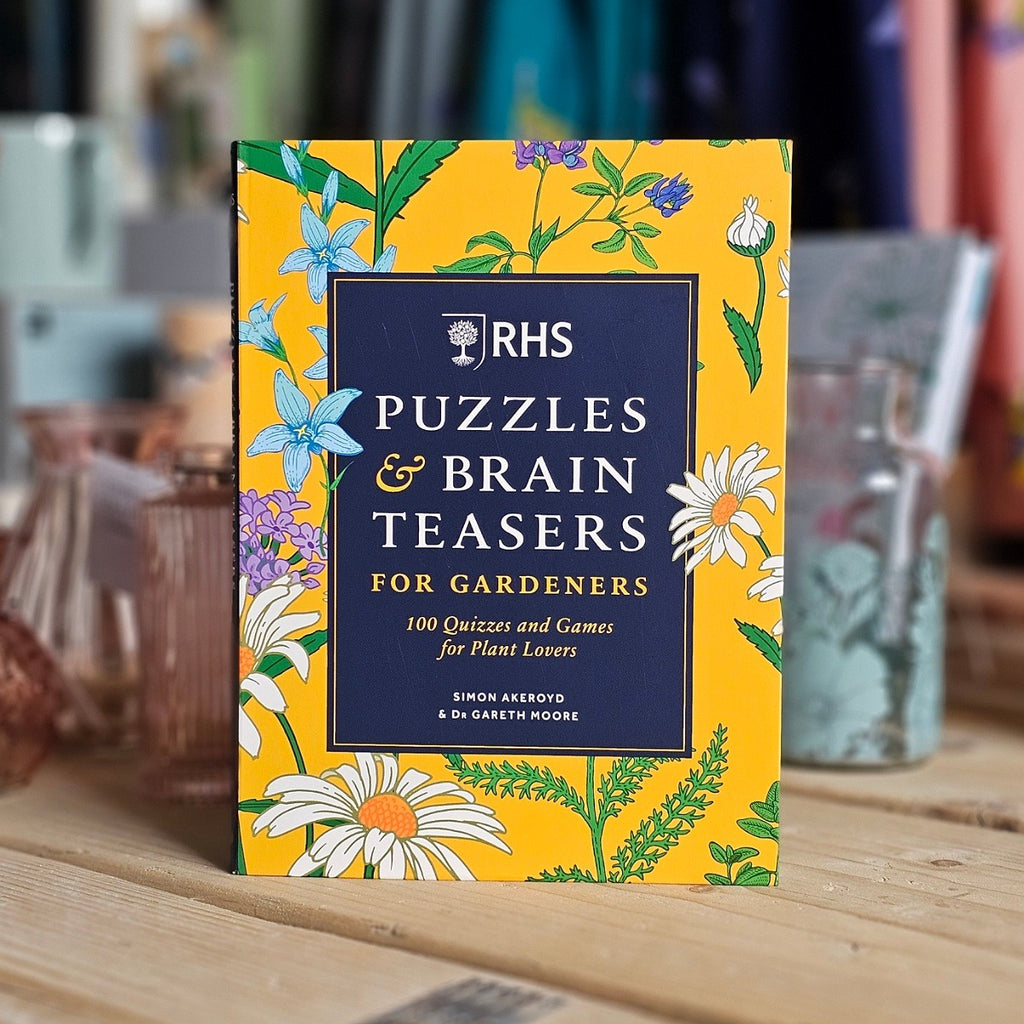 Book titled 'RHS Puzzles & Brain Teasers for Gardeners' on a wooden surface with a blurred background