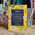 Book titled 'RHS Puzzles & Brain Teasers for Gardeners' on a wooden surface with a blurred background