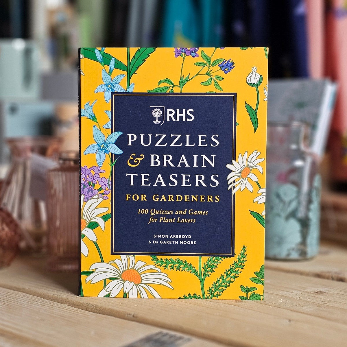 Book titled 'RHS Puzzles & Brain Teasers for Gardeners' on a wooden surface with a blurred background