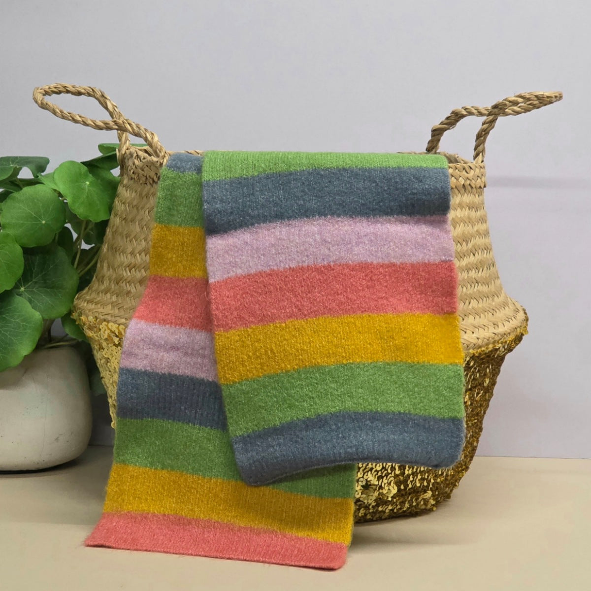 Colourful striped knit scarf draped over a woven basket with a plant in the background