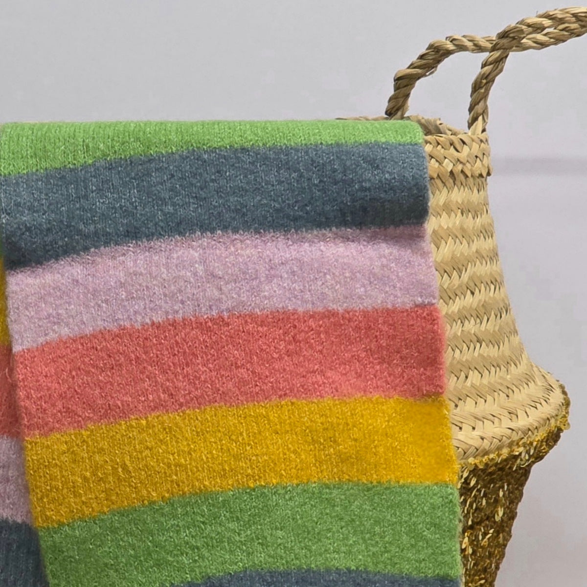 Colourful striped scarf draped over a wicker basket against a plain background