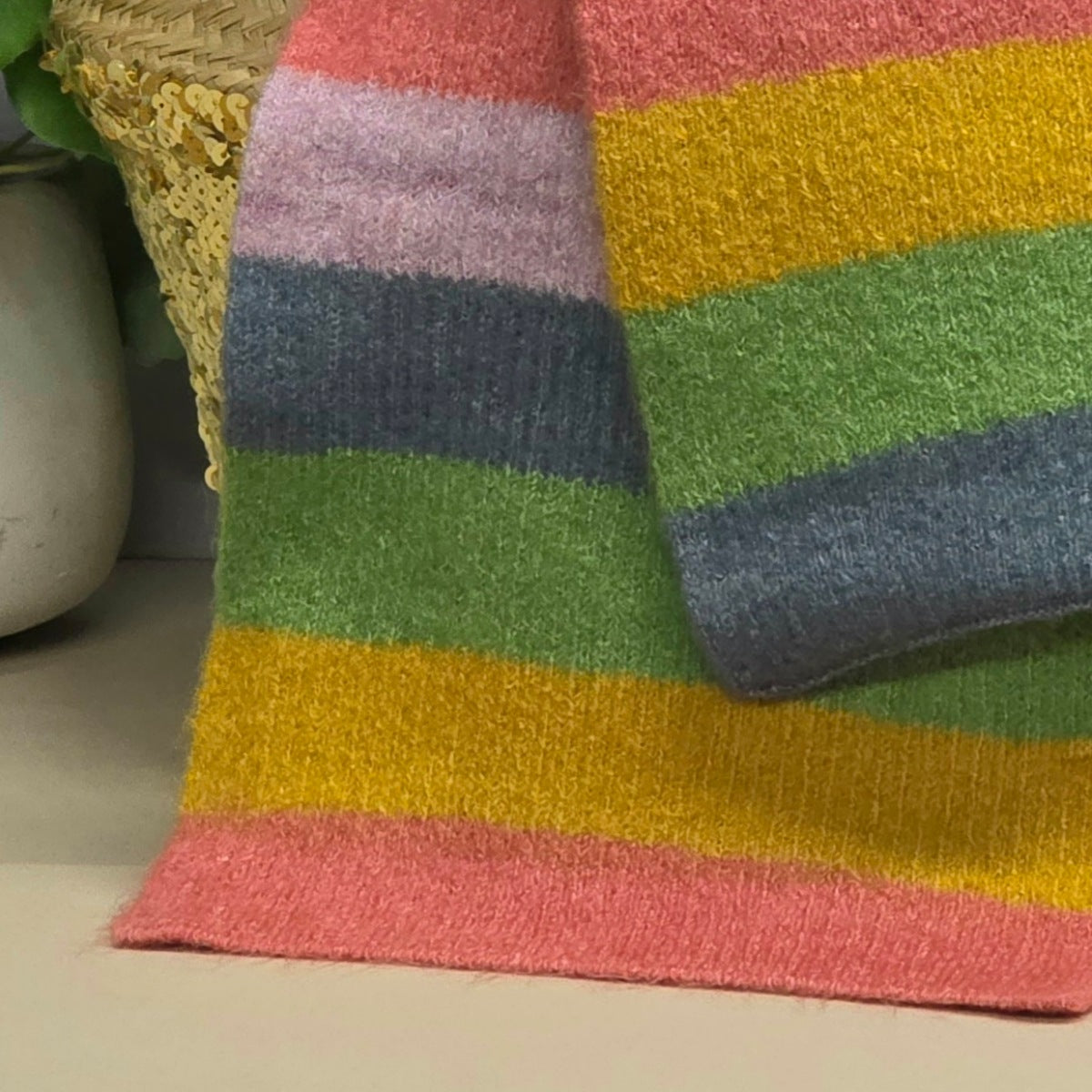 Close-up of a colourful striped knit scarf with a woven basket in the background.