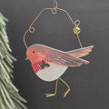 A Christmas wooden robin bird hanging ornament with a gold wire body and loop, featuring a red-breasted robin design with a red and white striped scarf and a small green holly accent, shown against a dark background.