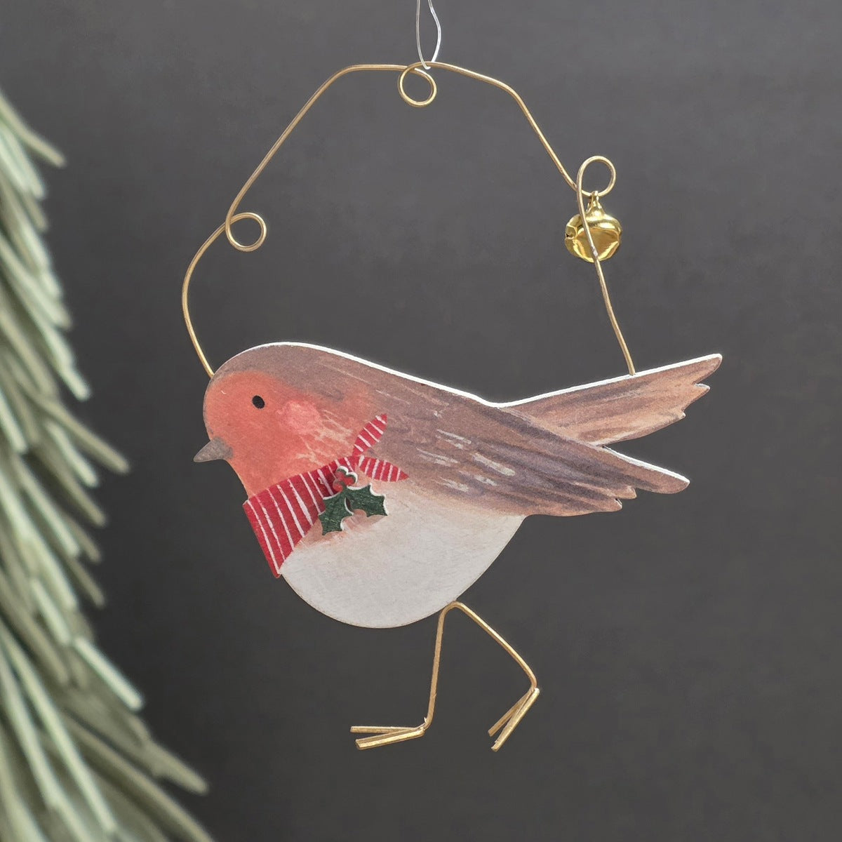 A Christmas wooden robin bird hanging ornament with a gold wire body and loop, featuring a red-breasted robin design with a red and white striped scarf and a small green holly accent, shown against a dark background.