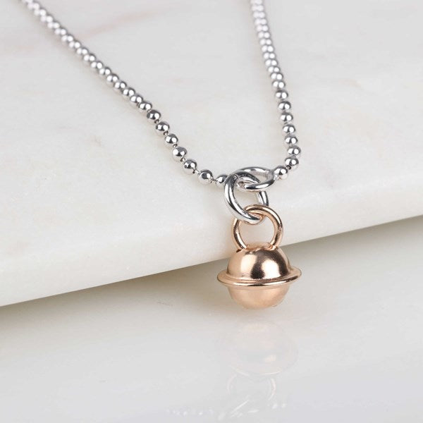 A silver beaded chain anklet with a small rose gold bell pendant, displayed on a white marble surface.
