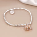A delicate beaded bracelet featuring small silver-toned round beads, a small round silver disc charm, and a polished rose gold elephant pendant, displayed on a warm beige surface.