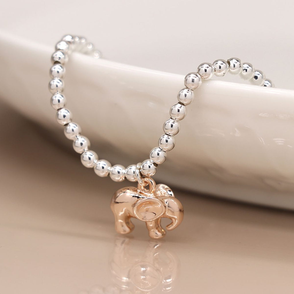 Silver beaded bracelet with a rose gold elephant charm on a beige surface