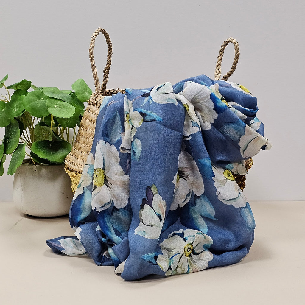 Denim blue scarf with floral-patterns in white, blue and yellow draped over a woven basket with a plant in the background