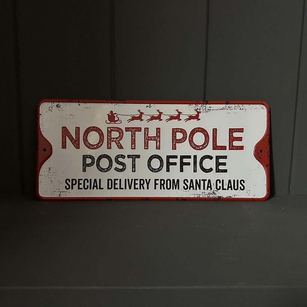 Vintage-style sign reading 'North Pole Post Office' with Santa's sleigh on a dark background