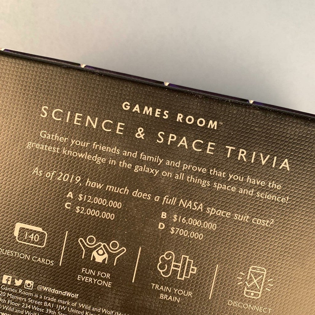 Close-up of the back of a Games Room Science & Space Trivia game box, showing printed trivia text and icons on a dark brown textured surface.