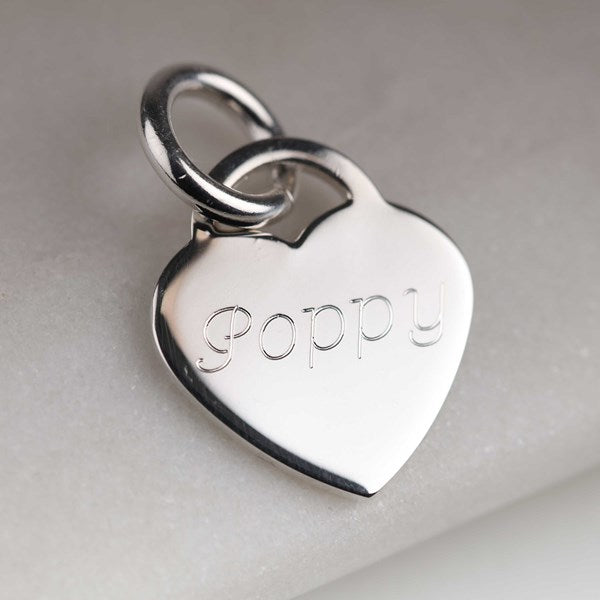 A polished silver heart-shaped charm engraved with the name 'Poppy', attached to a matching silver split ring, resting on a light gray textured surface.