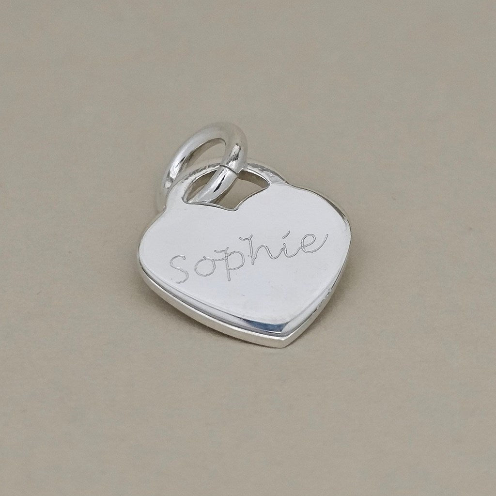 A sterling silver heart-shaped pendant charm engraved with the name 'Sophie' in cursive, resting on a neutral beige background.