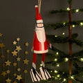 Red and white metal Santa Claus decoration with scuba diving mask, snorkel and flippers hanging on a string with a Christmas tree in the background.
