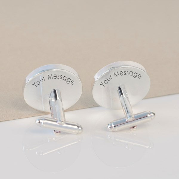 A pair of silver-toned cufflinks with oval backplates engraved with the text 'Your Message', displayed on a clean white surface with a beige background.