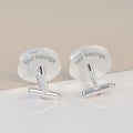A pair of silver-toned cufflinks with oval backplates engraved with the text 'Your Message', displayed on a clean white surface with a beige background.