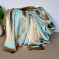 A reversible shimmering gold and light blue scarf with a contrasting boarder draped over a basket shown against a white background and potted plant to the side.