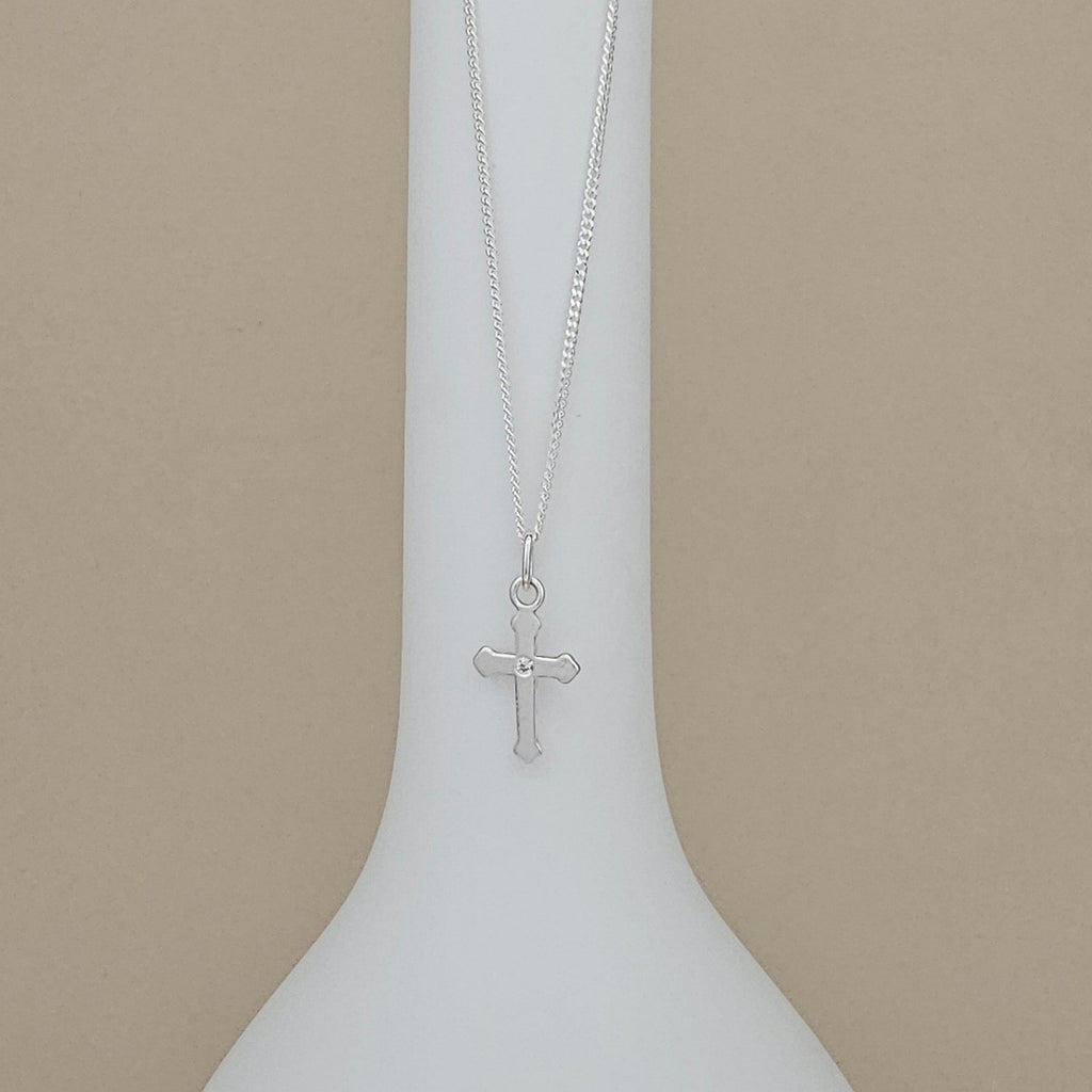 Silver cross necklace on a white stand with a beige background