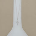 Silver cross necklace on a white stand with a beige background