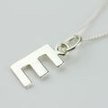 Silver necklace with a letter 'E' pendant on a light gray background