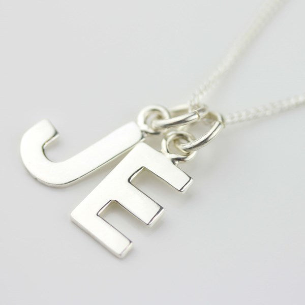 Silver necklace with a letter 'J' and 'E' pendant on a light gray background