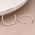 Silver hoop earrings with beaded detailing on a beige surface.