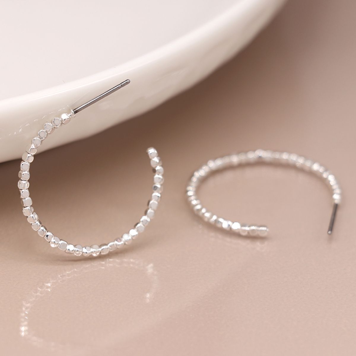 Silver hoop earrings with beaded detailing on a beige surface.