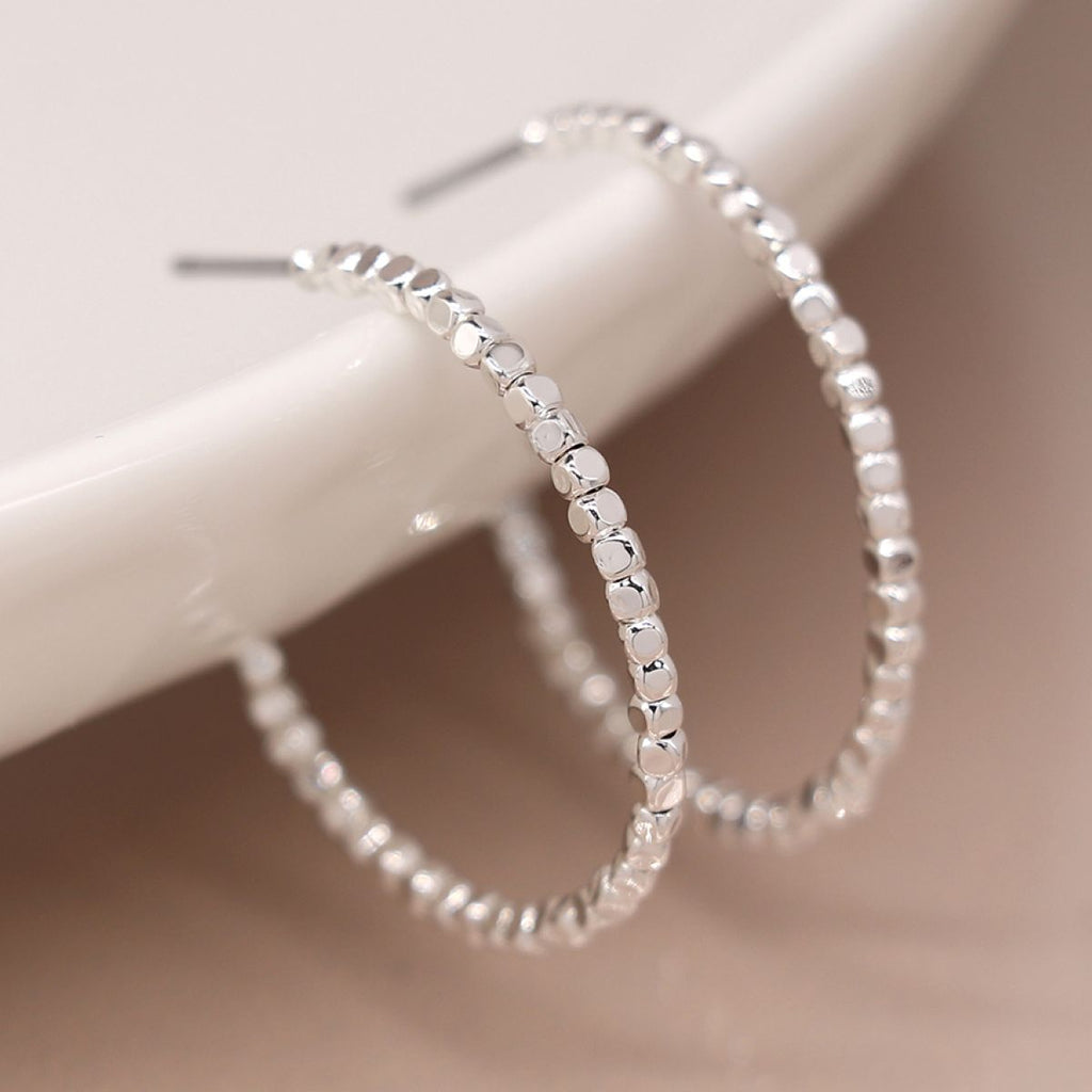 Silver hoop seed bead earrings on a white surface with a blurred background
