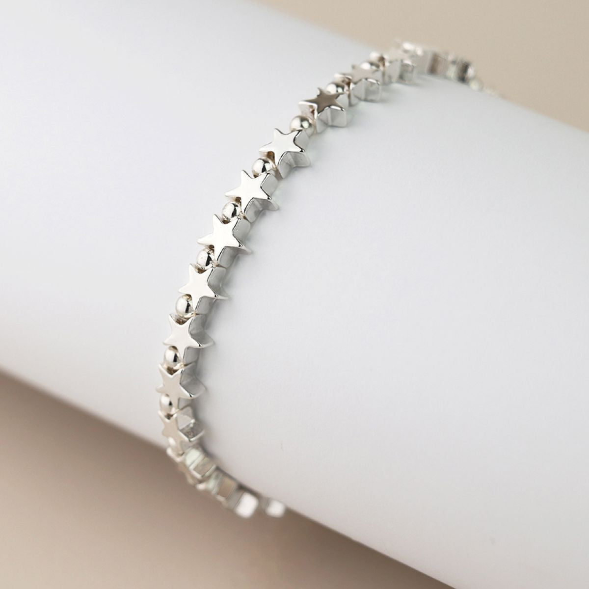 A silver star and bead linked bracelet displayed on a white cylindrical mannequin arm against a neutral beige background.