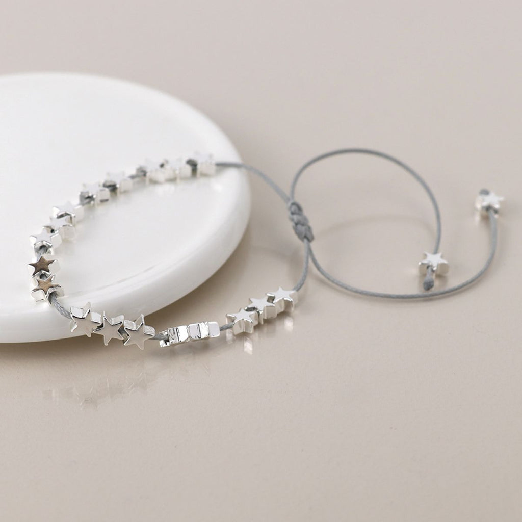 Silver cord bracelet with silver threaded star-shaped beads on a light beige background