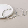 Silver cord bracelet with silver threaded star-shaped beads on a light beige background