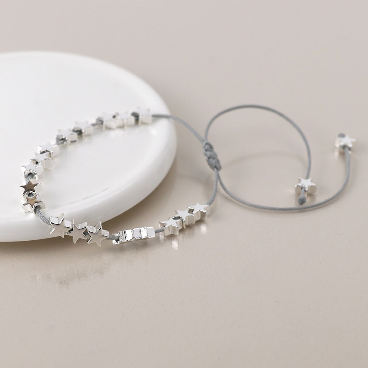 Silver cord bracelet with silver threaded star-shaped beads on a light beige background