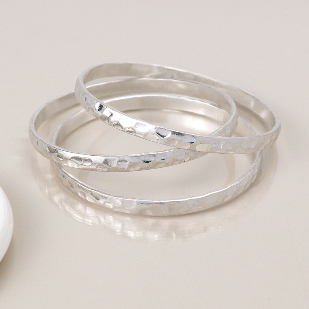 Three silver bangles on a light beige surface
