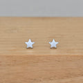 A pair of small silver star stud earrings resting on a light brown wooden surface against a neutral gray background.