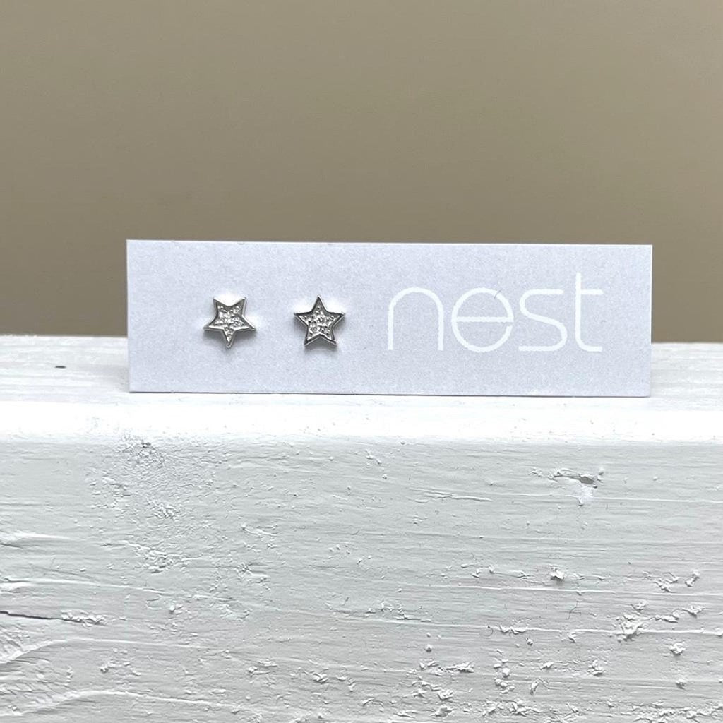 Star-shaped silver earrings on a 'nest' branded card against a beige background